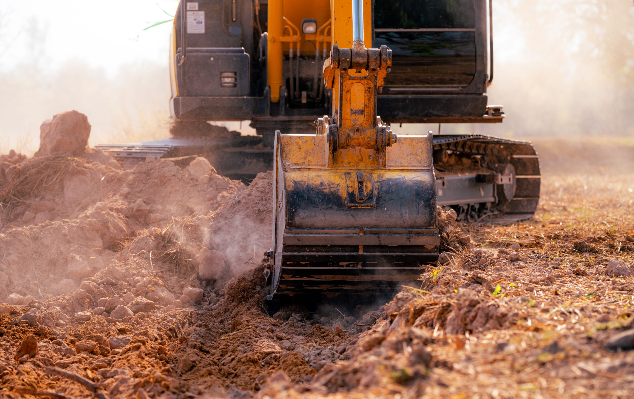 Metal bucket of backhoe digging soil. Excavator working at construction site. Earth moving machine. Excavation vehicle. Heavy machinery in action. Construction machinery and earth-moving equipment.